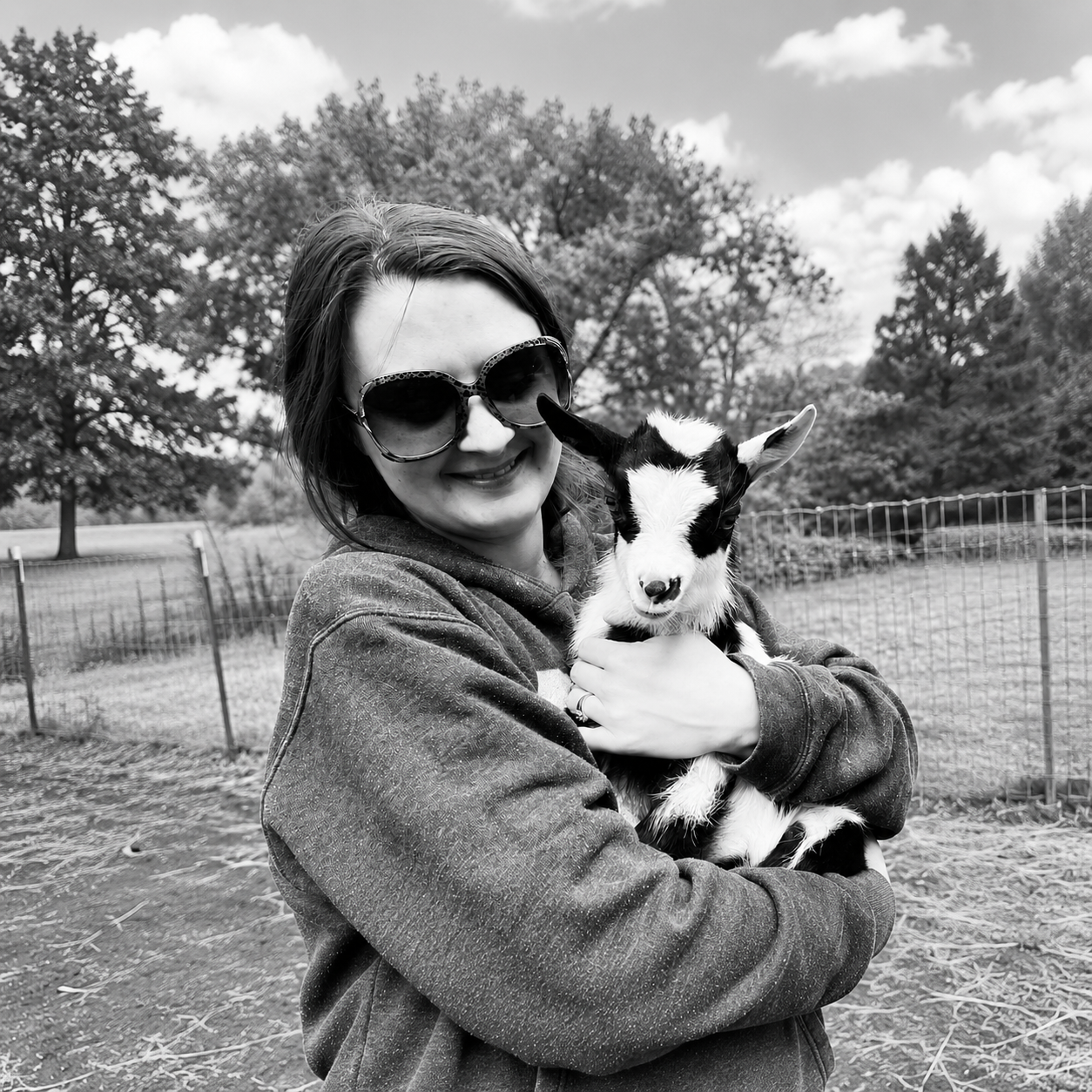 Sarah smiling while holding a young goat outdoors